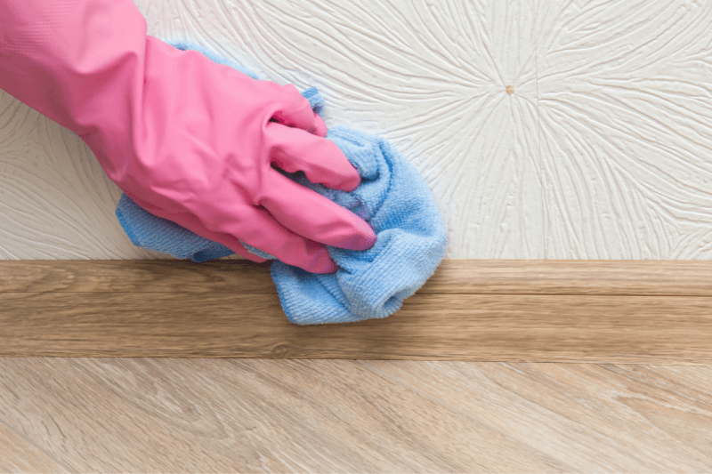 hand in pink glove cleaning baseboard on wooden floor