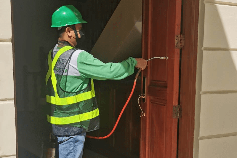 a pest control doing termite treatment on a wooden door - How to protect your home from termite damage
