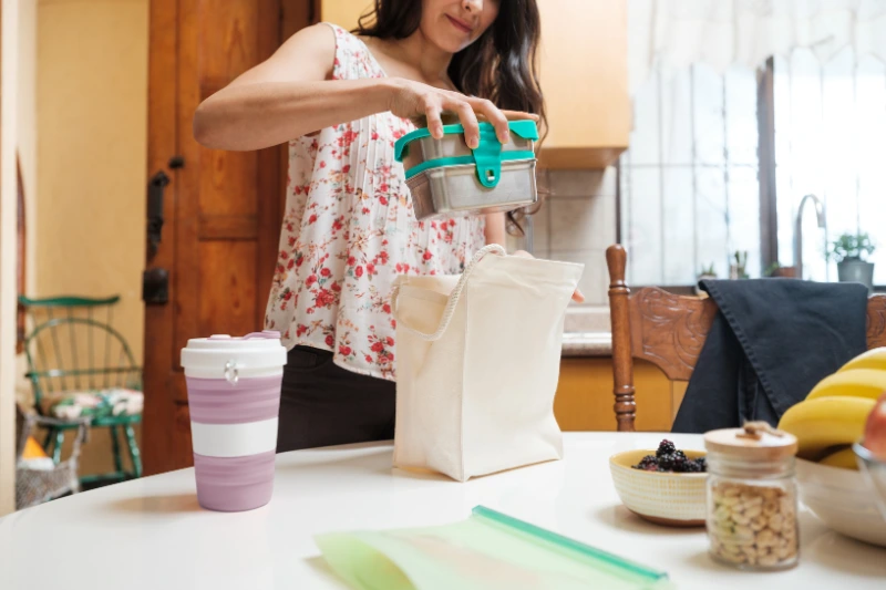 Start the Year Right: Your Easy Guide to a New Year 2024_A woman taking lunch in<br />
reusable containers and putting them<br />
in a bag made of fabric for a<br />
sustainable lifestyle.