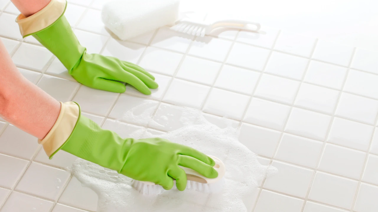 A person with green gloves diligently cleans a tile floor, enhancing home hygiene to reduce pest attraction.