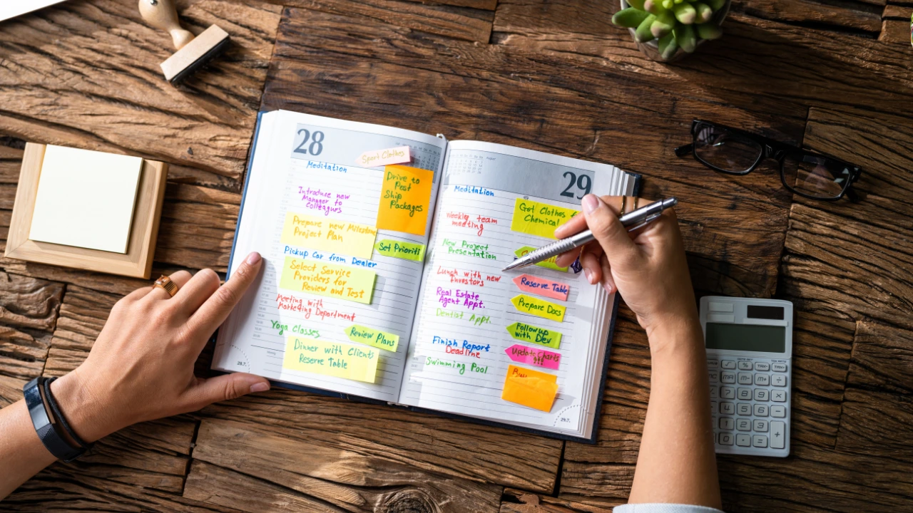 A woman writes pest control resolutions on a calendar using a pen and paper, seated at a wooden table.