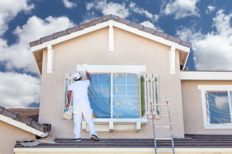 A man performing home maintenance by painting a window on a house, ensuring its upkeep and aesthetic appeal.