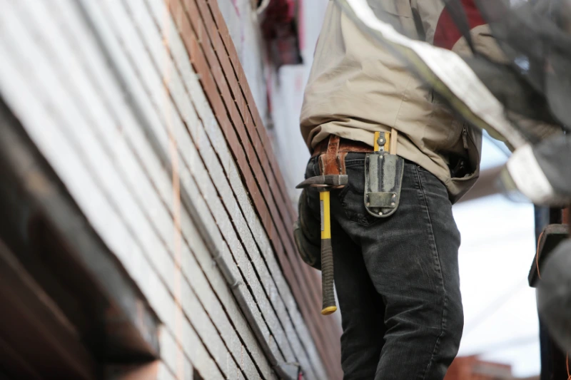 A man on a ladder wearing a tool belt, engaged in home maintenance tasks.