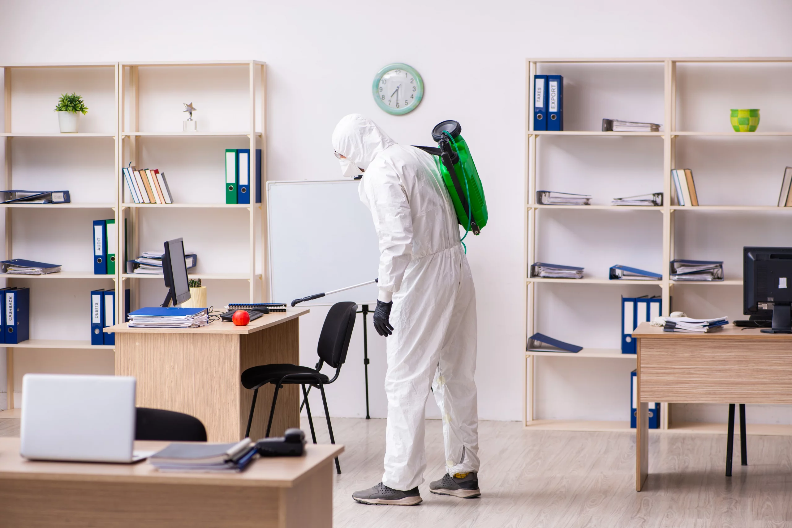 A man in a white suit and green backpack cleans a room, implementing pest control measures to prevent infestations for workplace pest prevention.