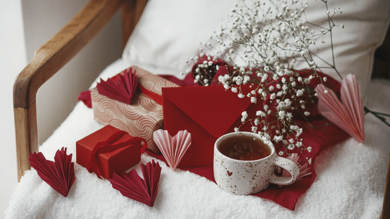 A cup of coffee, a red heart, and a gift box on a bed, symbolizing a cozy and clean Valentine's Day atmosphere.